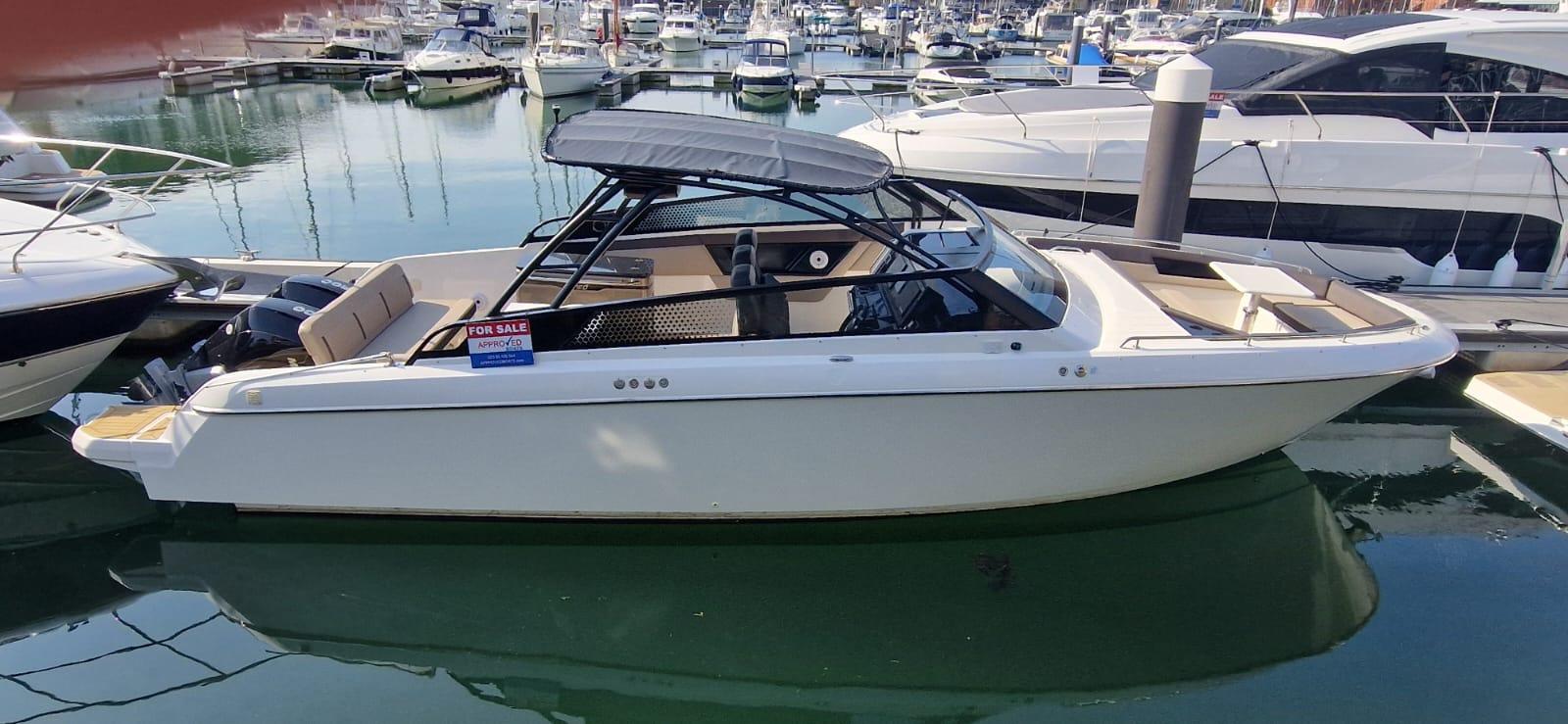 A white boat with a canopy docked at a marina, featuring 'FOR SALE' signage and visible reflections in the water.